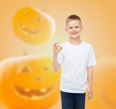 holidays, childhood, happiness, gesture and people concept - smiling little boy in white blank shirt showing ok sign over halloween pumpkins background