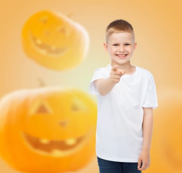 holidays, childhood, happiness, gesture and people concept - smiling little boy in white blank shirt pointing finger at you over halloween pumpkins background