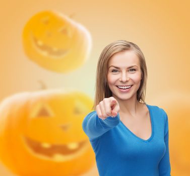 gesture, holidays and people concept - smiling young woman pointing finger at you over pumpkins background