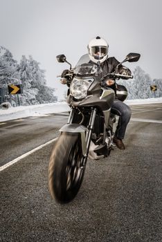 Biker in helmet and leather jacket riding on the road with snow.