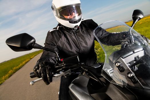 Biker in helmet and leather jacket riding on the road.