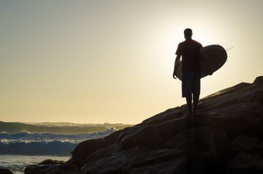 A surfer watching the waves at sunset in Portugal.