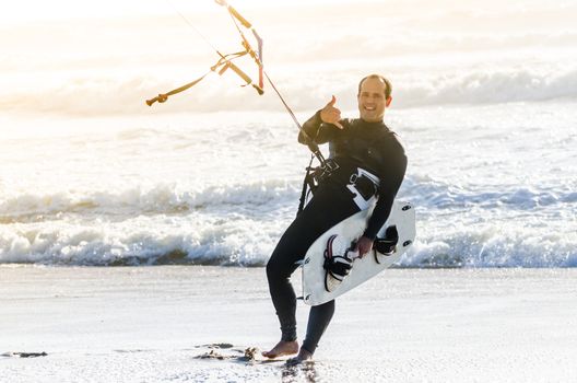 Kitesurfer smiling and waving to the camera on a beautiful background of spray during the sunset.