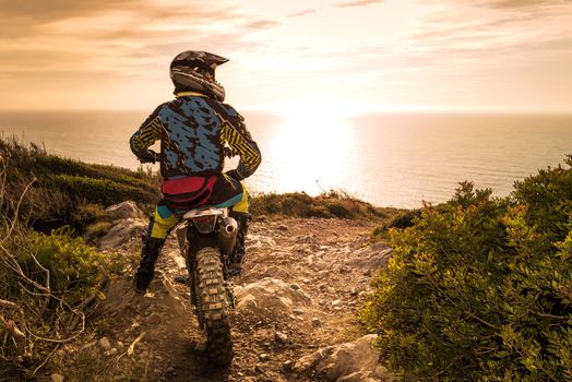 Enduro racer sitting on his motorcycle watching the sunset.