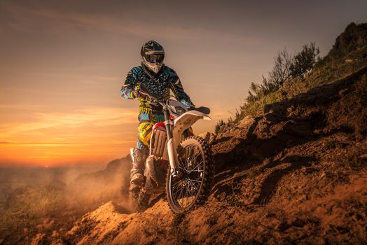 enduro rider climbing a high slope against a beautiful sunset on a seascape.