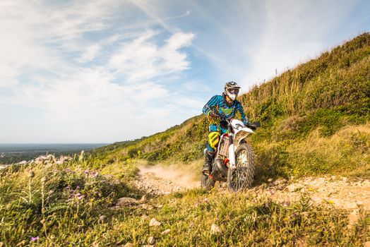 Enduro rider climbing a steep slope against a sunset sky.