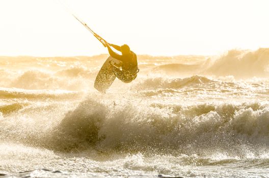 Kitesurfer jumping on a beautiful background of spray during the sunset.