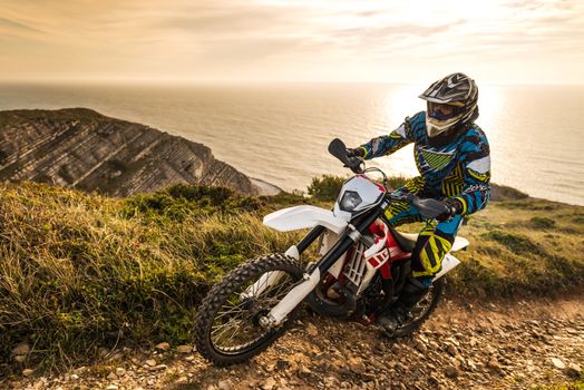 Enduro rider climbing a steep slope against a beautiful sunset on a seascape