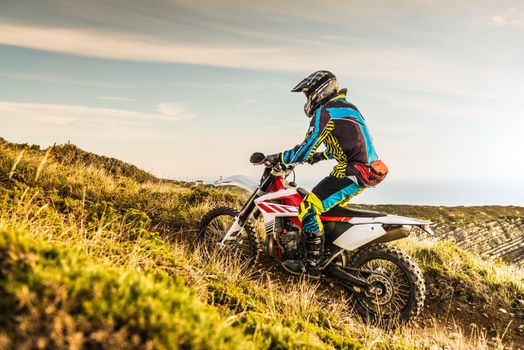 Enduro rider climbing a steep slope against a sunset sky.