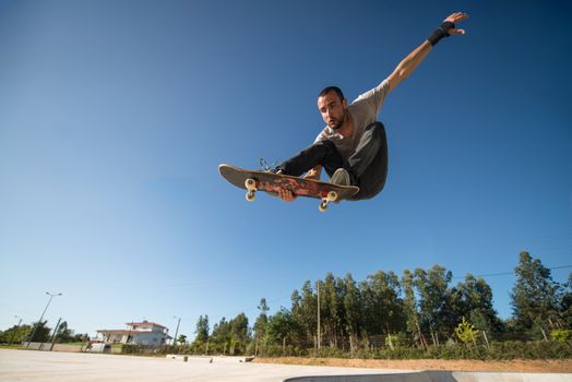 Skateboarder flying over a ramp on blue clear sky.