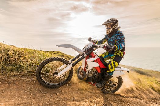 Enduro rider climbing a steep slope against a beautiful sunset on a seascape