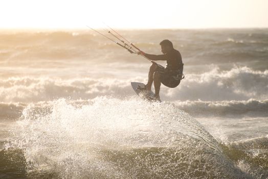 Kitesurfer jumping on a beautiful background of spray during the sunset.