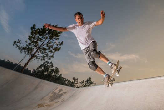 Skateboarder in a concrete pool at skatepark on a beatiful sunset.