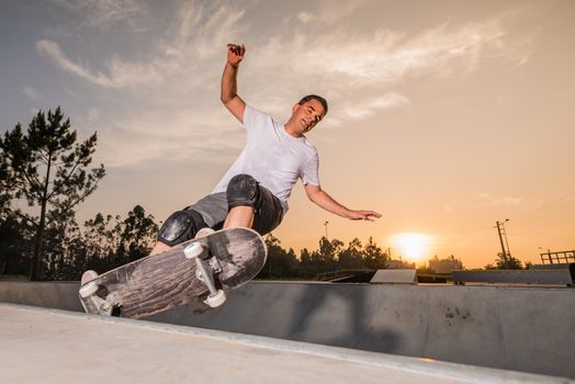 Skateboarder in a concrete pool at skatepark on a beatiful sunset.