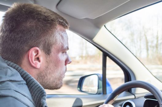 Young man driving a car, holding his right hand on the steering wheel.