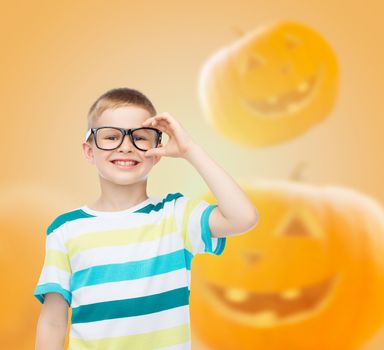 education, holidays, childhood, vision and people concept - smiling little boy in glasses over halloween pumpkins background