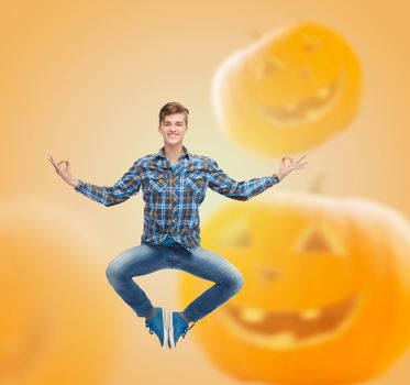 happiness, freedom, holidays and people concept- smiling young man jumping in air over halloween pumpkins background