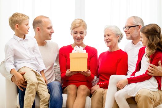 family, holidays, generation, christmas and people concept - smiling family with gift box sitting on couch at home