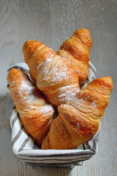 fresh croissants in basket on wooden table