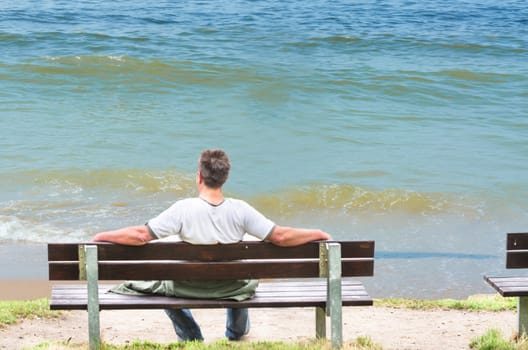 Man sitting alone on a bench overlooking the sea.