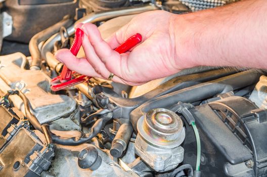 Hand of an auto mechanic in the engine compartment in the car-repair workshop.