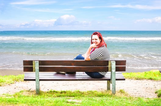 Young Woman sitting alone on a bench overlooking the sea.