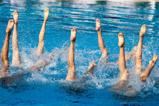 Synchronized swimmers' legs in the swimming pool. Summer sport.