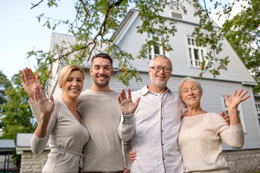 family, generation, home, gesture and people concept - happy family standing in front of house waving hands outdoors