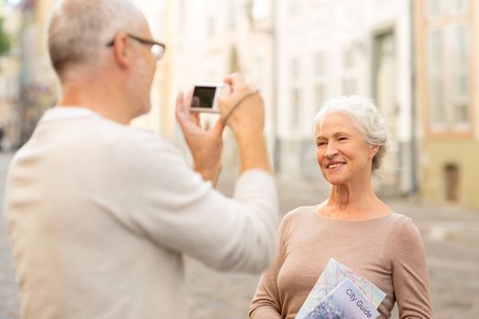 age, tourism, travel, technology and people concept - senior couple with map and camera photographing on street