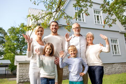 family, generation, gesture, home and people concept - happy family standing in front of house waving hands outdoors