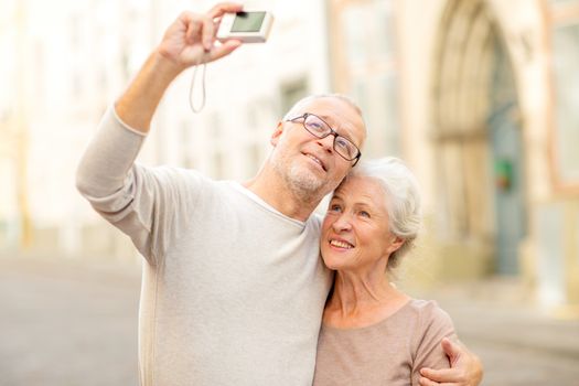 age, tourism, travel, technology and people concept - senior couple with camera taking selfie on street