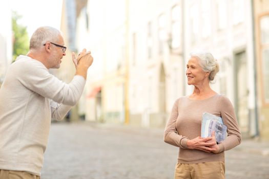 age, tourism, travel, technology and people concept - senior couple with map and camera photographing on street