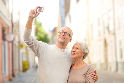 age, tourism, travel, technology and people concept - senior couple with camera taking selfie on street