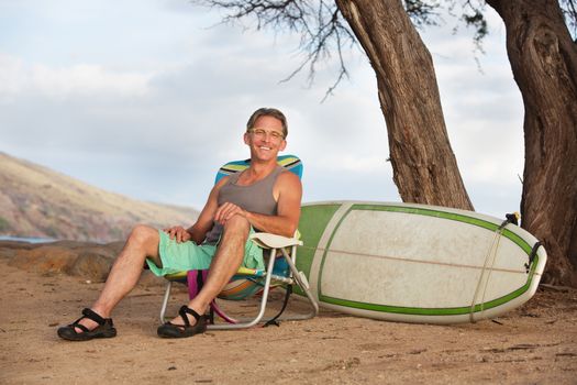 Single cheerful athletic male sitting with surfboard
