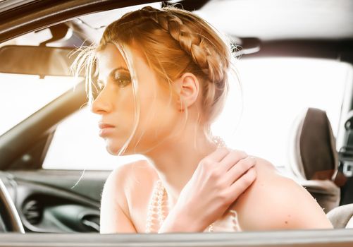 Young Woman in a pearl necklace sat In the drivers seat of her car