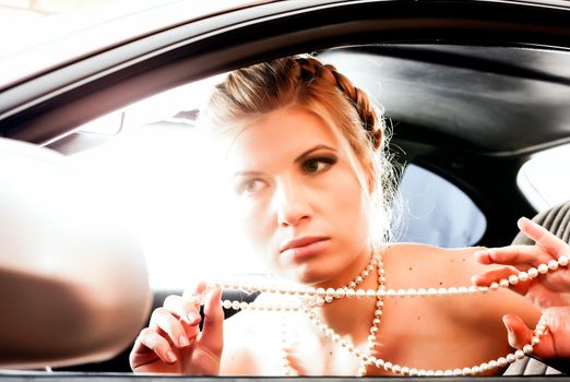 Young Woman in a pearl necklace sat In the drivers seat of her car