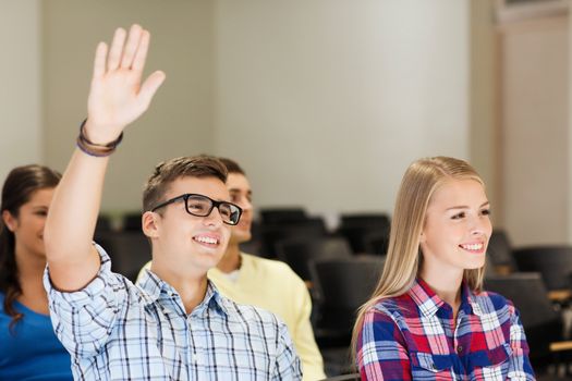 education, high school, teamwork and people concept - group of smiling students raising hand in lecture hall