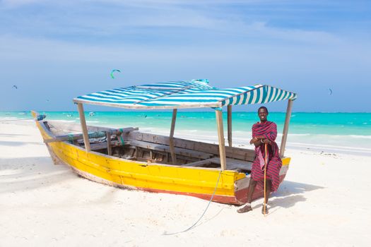 Maasai warrior lounging aroundon traditional colorful wooden boat on picture perfect tropical sandy beach on Zanzibar, Tanzania, East Africa. Kiteboarding spot on Paje beach.