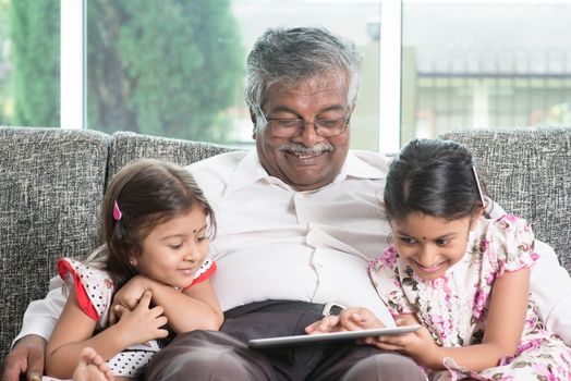 Modern technology concept. Grandparent and grandchildren using touch screen tablet computer. Portrait Indian family at home. Asian people living lifestyle.