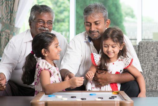 Happy multi generations Asian Indian family playing carom game at home. Grandparent, parent and children indoor lifestyle.