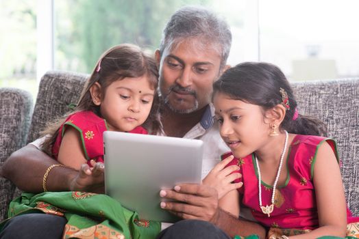 Modern technology concept. Indian family at home. Asian father and children using touch screen tablet computer, sitting on sofa, home schooling concept.