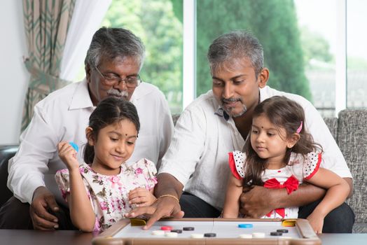 Happy multi generations Asian Indian family playing carrom game at home. Grandparent, parent and children indoor lifestyle.