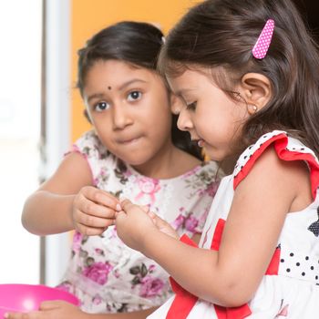 Indian girls sharing traditional snack murukku with each other. Asian sibling or children eating food, living lifestyle at home.