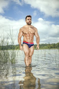 An image of a muscular man in the lake with a white shirt and sunglasses