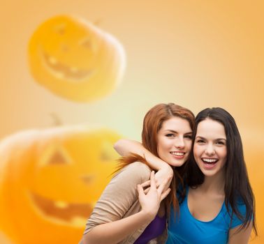 happiness, holidays, friendship and people concept - smiling teenage girls hugging over halloween pumpkins background