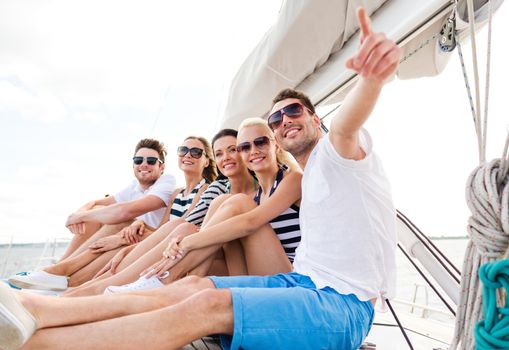 vacation, travel, sea, friendship and people concept - smiling friends sitting on yacht deck and pointing finger