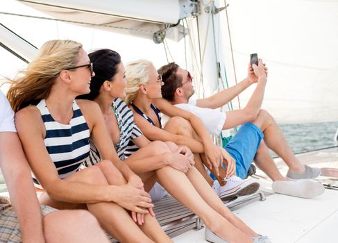 vacation, travel, sea, friendship and people concept - smiling friends sitting on yacht deck and making selfie