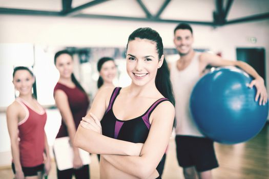 fitness, sport, training, gym and lifestyle concept - smiling woman standing in front of the group of people in gym