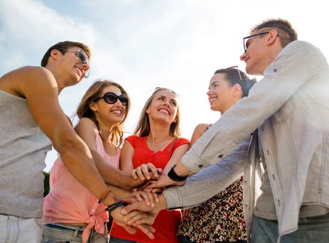 friendship, leisure, summer, gesturer and people concept - group of smiling friends with hands on top in city