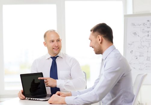 business, technology and office concept - two smiling businessmen with laptop having presentation in office